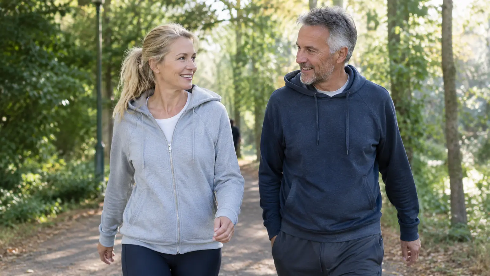 A woman in her late 50s walking outdoors on a tree-lined path in the morning with a companion